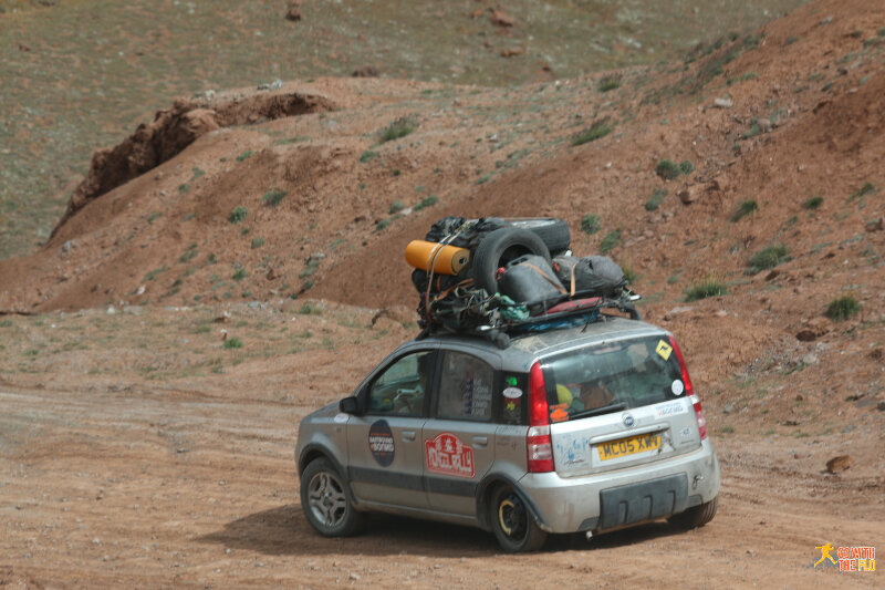 Mongol rallye car with four Australians inside, driving on a spare tire with a broken suspension.